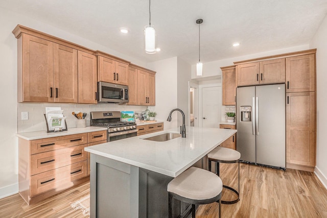 kitchen with sink, hanging light fixtures, a center island with sink, light hardwood / wood-style flooring, and appliances with stainless steel finishes