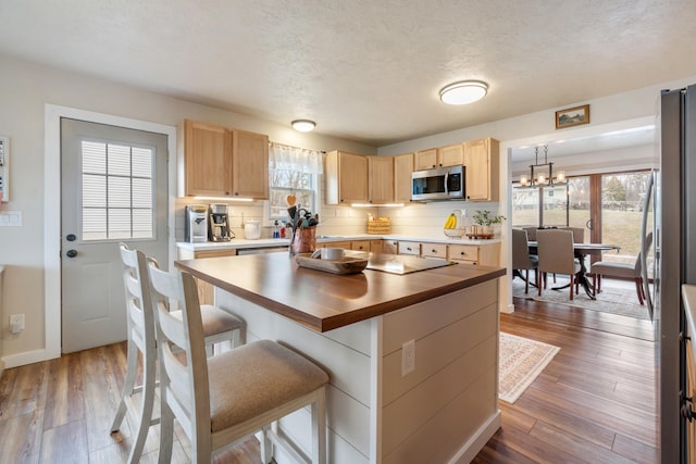 kitchen with butcher block countertops, a breakfast bar area, hanging light fixtures, stainless steel appliances, and hardwood / wood-style floors