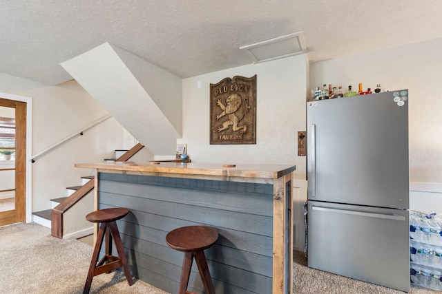 kitchen featuring stainless steel refrigerator, light colored carpet, a breakfast bar, and a textured ceiling