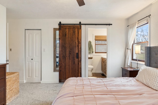 carpeted bedroom featuring a closet, ensuite bath, a barn door, and ceiling fan