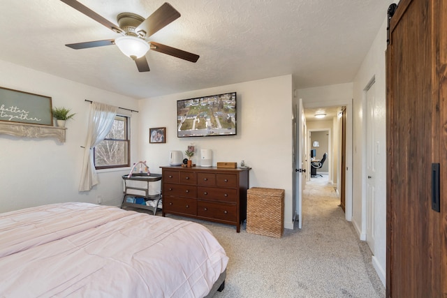 bedroom featuring light carpet, ceiling fan, a barn door, and a textured ceiling