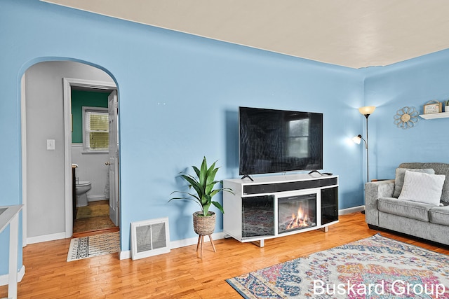 living area with arched walkways, hardwood / wood-style flooring, visible vents, baseboards, and a glass covered fireplace