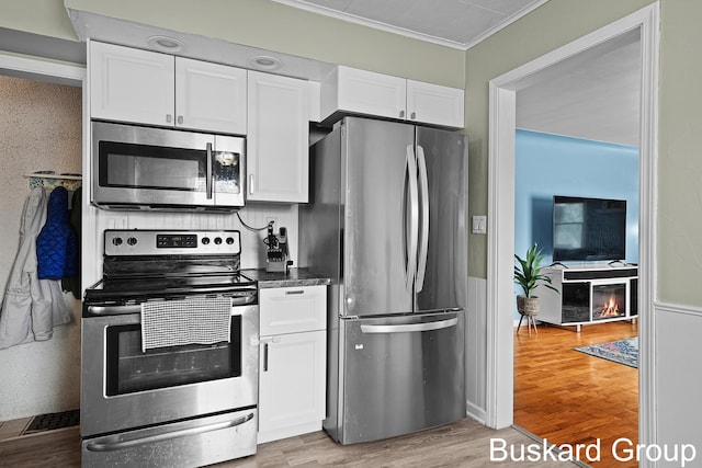 kitchen featuring dark countertops, appliances with stainless steel finishes, crown molding, light wood-type flooring, and white cabinetry