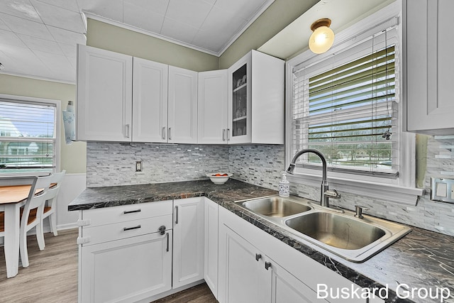 kitchen with white cabinets, glass insert cabinets, ornamental molding, a sink, and backsplash