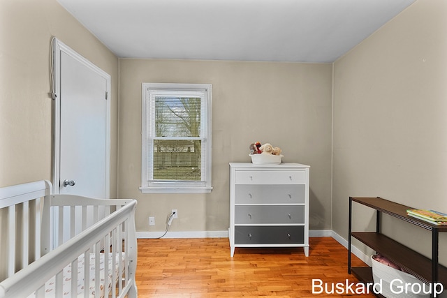 bedroom with light wood-type flooring, a nursery area, and baseboards