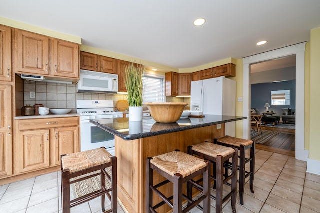 kitchen with white appliances, a kitchen bar, light tile patterned floors, and a center island