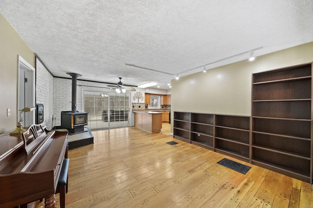 living room with ceiling fan, a textured ceiling, light hardwood / wood-style flooring, and a wood stove