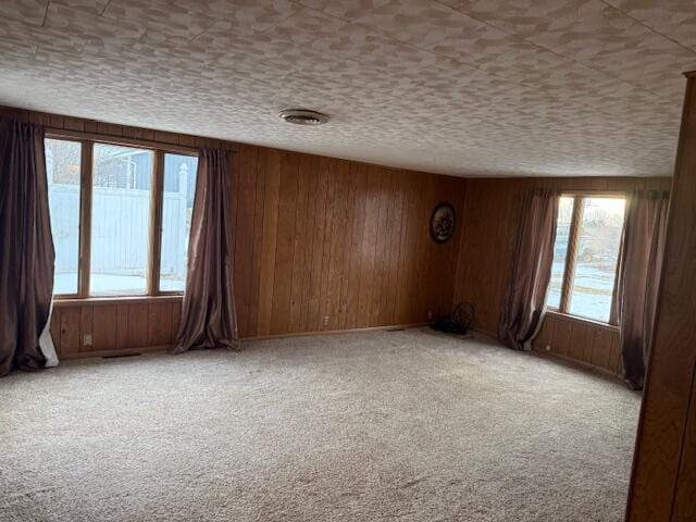 carpeted empty room with wooden walls and a textured ceiling