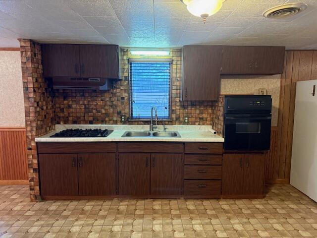 kitchen with dark brown cabinets, sink, wooden walls, and black appliances