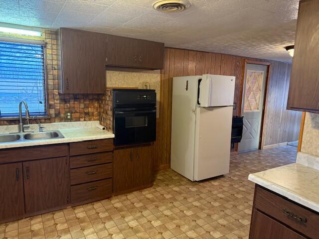 kitchen featuring sink, backsplash, wooden walls, oven, and white fridge