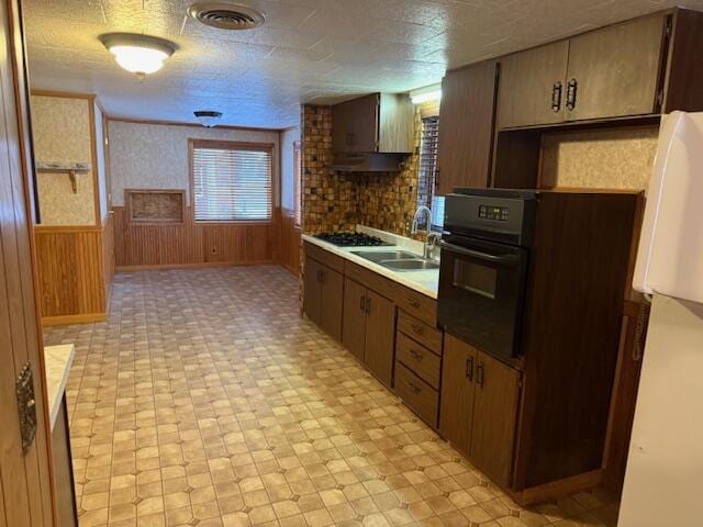 kitchen with sink, black oven, wood walls, a textured ceiling, and white fridge