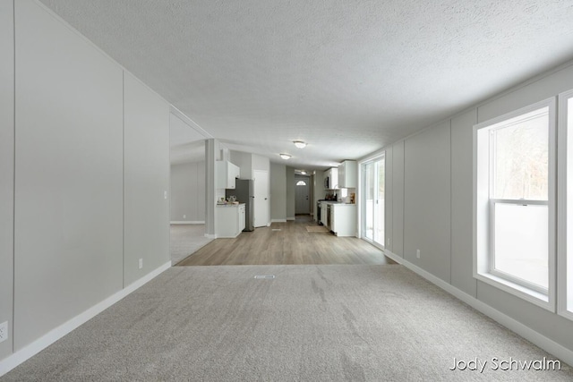 unfurnished living room featuring plenty of natural light, light colored carpet, and a textured ceiling