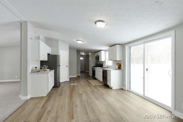 kitchen featuring sink, white cabinetry, a textured ceiling, light hardwood / wood-style flooring, and appliances with stainless steel finishes