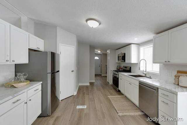 kitchen featuring sink, light hardwood / wood-style flooring, appliances with stainless steel finishes, white cabinetry, and tasteful backsplash