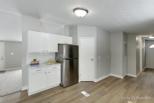 kitchen with light hardwood / wood-style flooring, stainless steel refrigerator, a textured ceiling, white cabinets, and decorative backsplash