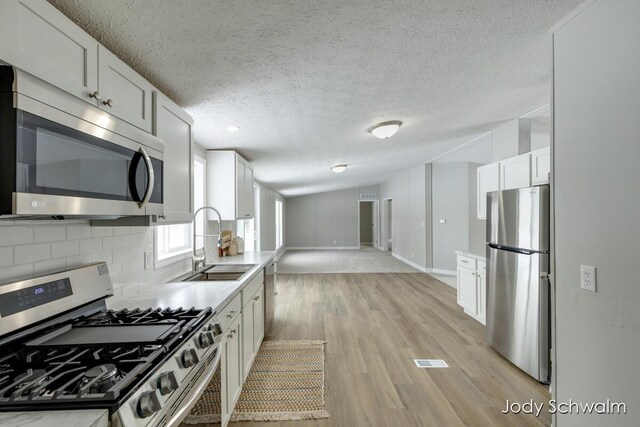 kitchen with stainless steel appliances, white cabinetry, sink, and backsplash