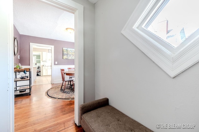 corridor with a textured ceiling and light hardwood / wood-style flooring