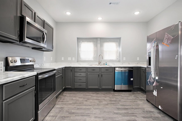 kitchen featuring sink, light stone counters, gray cabinets, stainless steel appliances, and light hardwood / wood-style floors