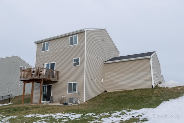 snow covered back of property featuring a deck and a lawn