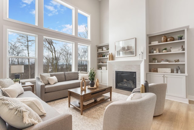 living room featuring a healthy amount of sunlight, built in features, light hardwood / wood-style floors, and a towering ceiling