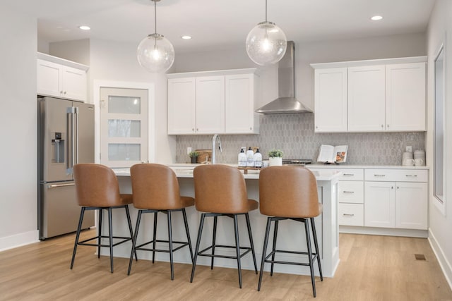 kitchen with white cabinets, high quality fridge, decorative light fixtures, and wall chimney range hood