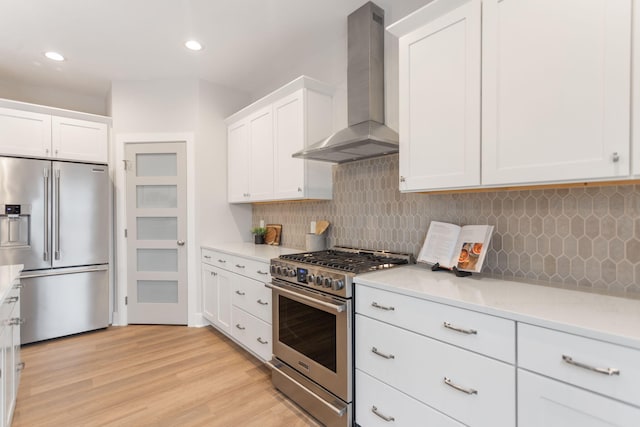 kitchen with white cabinetry, wall chimney range hood, light hardwood / wood-style floors, and appliances with stainless steel finishes