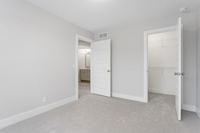 unfurnished bedroom with a walk in closet, light colored carpet, and a closet