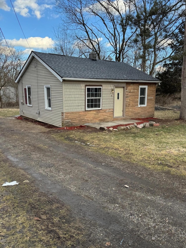 view of front of house with a shingled roof, stone siding, and driveway