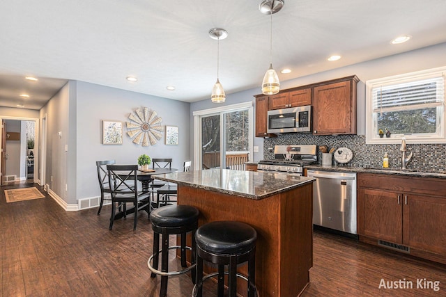 kitchen with stainless steel appliances, decorative light fixtures, a kitchen island, backsplash, and dark wood-type flooring