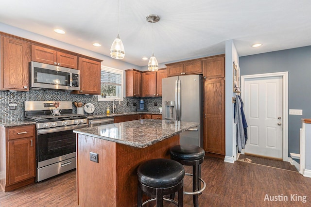 kitchen featuring sink, a center island, pendant lighting, dark stone counters, and stainless steel appliances