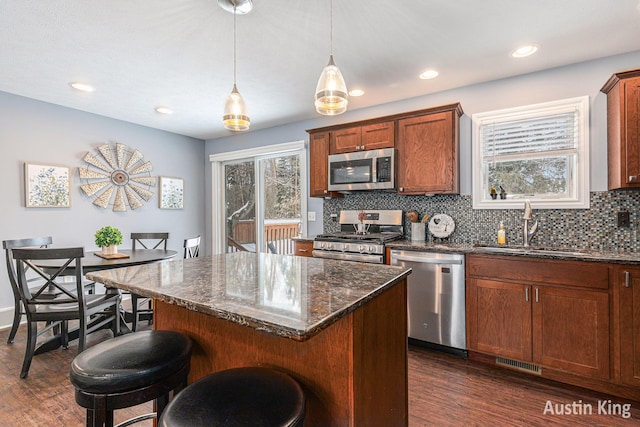 kitchen with appliances with stainless steel finishes, pendant lighting, a center island, sink, and dark stone countertops