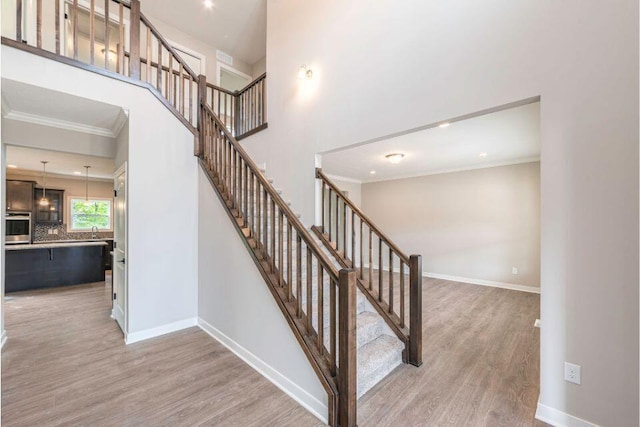 staircase featuring crown molding, sink, hardwood / wood-style flooring, and a towering ceiling