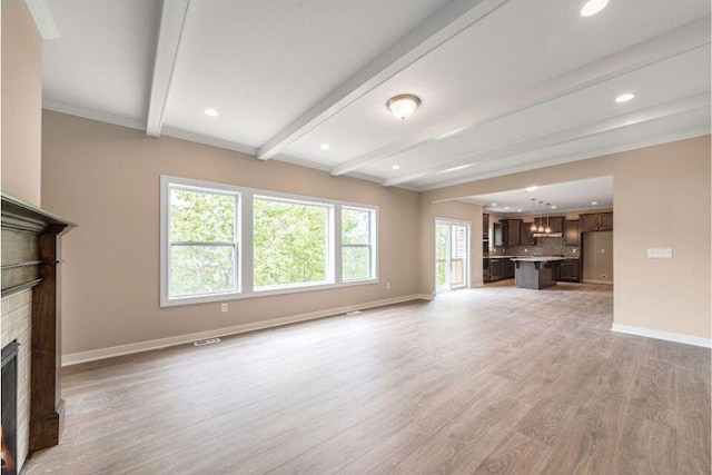 unfurnished living room with beamed ceiling, a brick fireplace, and light wood-type flooring