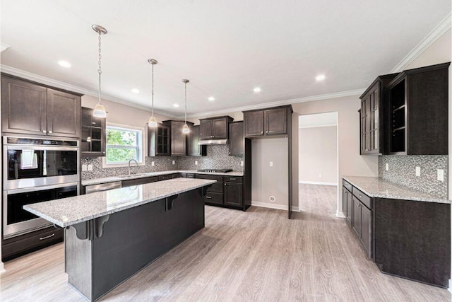 kitchen with sink, appliances with stainless steel finishes, a kitchen breakfast bar, a center island, and light stone counters