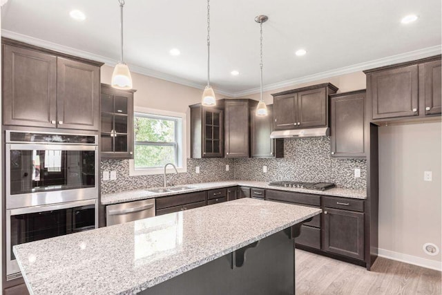 kitchen with sink, hanging light fixtures, stainless steel appliances, a center island, and light stone counters