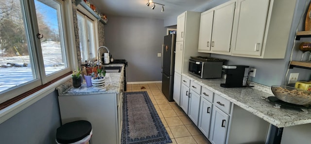 kitchen featuring light tile patterned flooring, sink, white cabinetry, stainless steel appliances, and light stone countertops