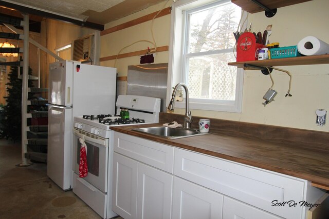 kitchen with concrete flooring, sink, white cabinets, wooden counters, and white appliances