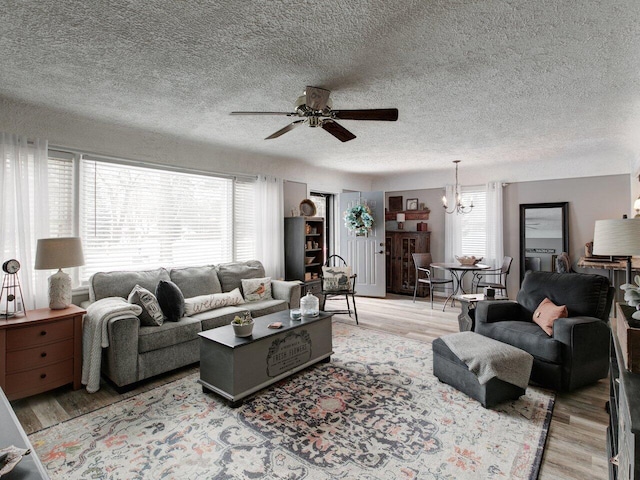 living room with ceiling fan with notable chandelier, light hardwood / wood-style flooring, and a textured ceiling