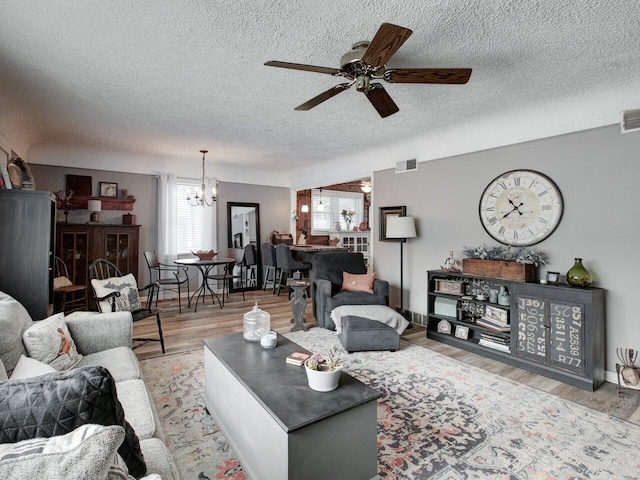 living room with ceiling fan with notable chandelier, a textured ceiling, and light wood-type flooring