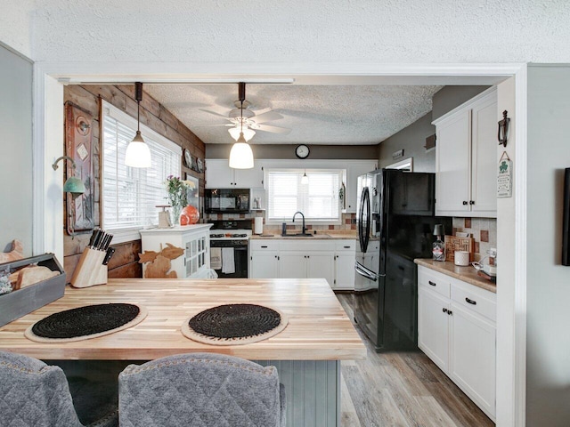 kitchen with pendant lighting, black appliances, light hardwood / wood-style floors, white cabinets, and wood counters