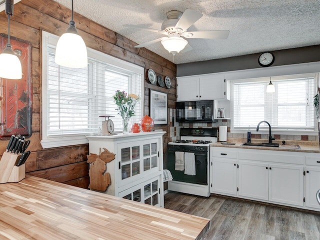 kitchen featuring sink, range with gas cooktop, white cabinetry, hanging light fixtures, and light wood-type flooring