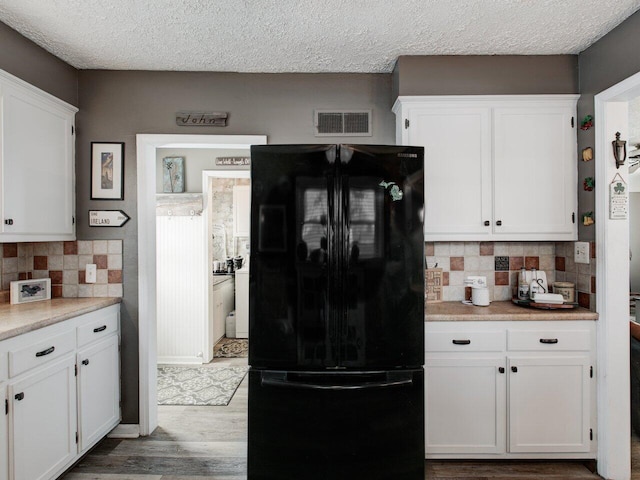 kitchen featuring hardwood / wood-style flooring, black fridge, and white cabinets