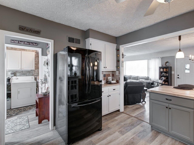 kitchen with black refrigerator, white cabinetry, washer / clothes dryer, and decorative light fixtures