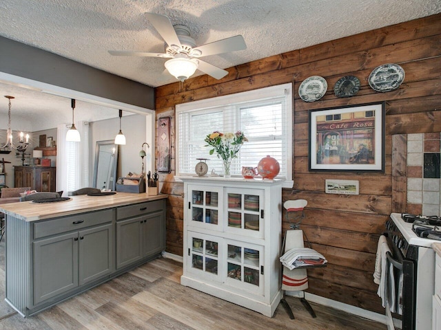 kitchen featuring hanging light fixtures, a textured ceiling, light hardwood / wood-style floors, gas range oven, and ceiling fan with notable chandelier