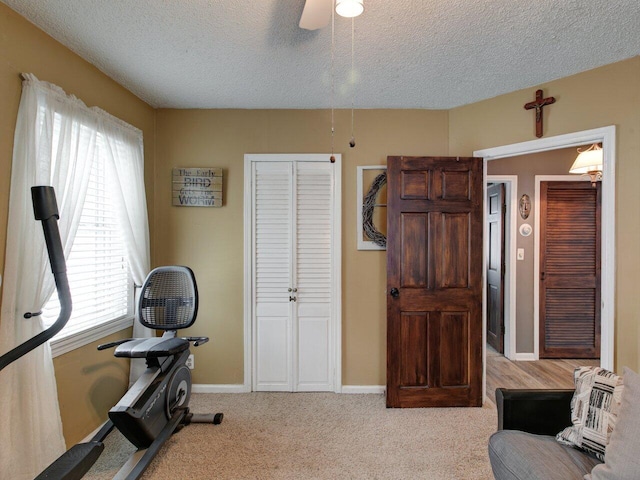 exercise area with ceiling fan, a wealth of natural light, light colored carpet, and a textured ceiling