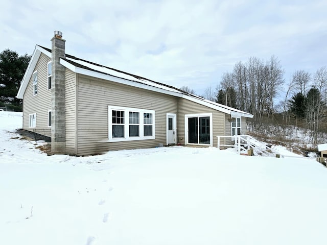 snow covered rear of property with a chimney