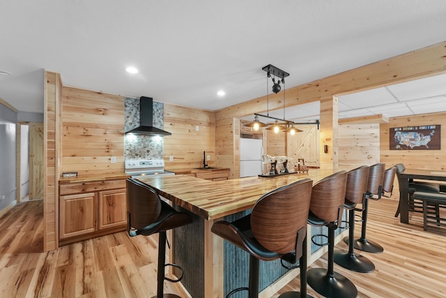 bar with sink, butcher block countertops, white refrigerator, pendant lighting, and wall chimney range hood