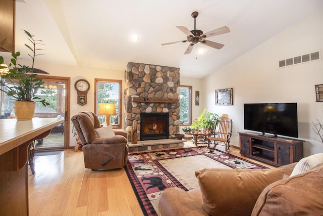 living room with ceiling fan, high vaulted ceiling, a stone fireplace, and light hardwood / wood-style floors