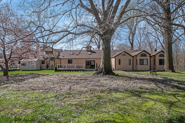 rear view of house with a chimney, a wooden deck, and a lawn