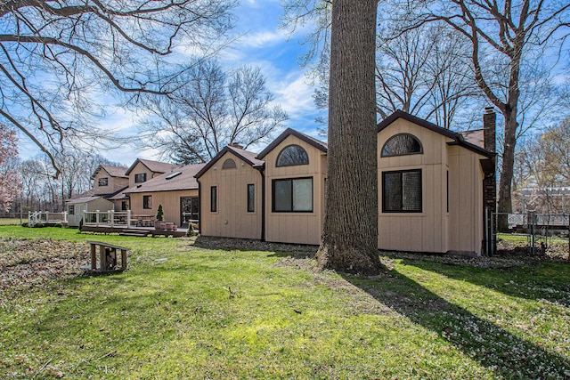 back of house featuring a chimney, a lawn, a deck, and fence
